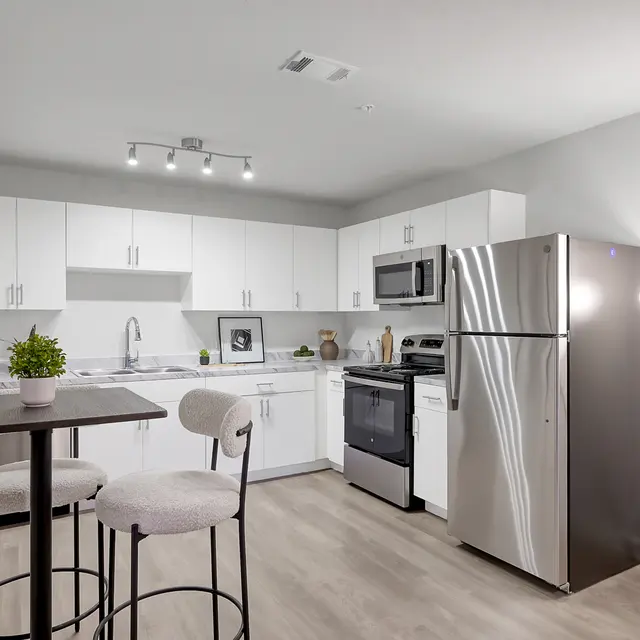 A modern kitchen featuring white cabinetry, stainless steel appliances, and a small dining table with two stools.