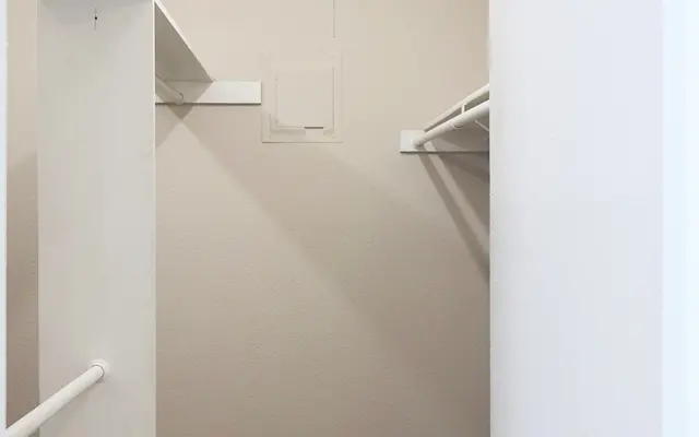 An empty closet with two hanging rods and neutral-colored walls.