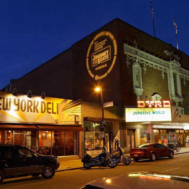 A nighttime view of carytown va street featuring famous Byrd Theater and Deli. The building is illuminated with warm lights against a dark sky.