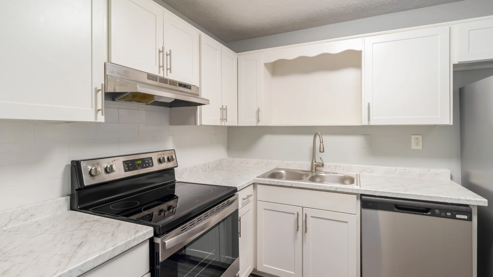 Modern kitchen featuring white cabinetry, marble countertops, stainless steel appliances, and a single bowl sink.