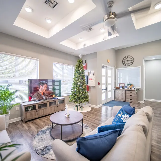 A cozy modern living room decorated for the holidays with a Christmas tree, a television showing a holiday movie, and a comfortable seating area.