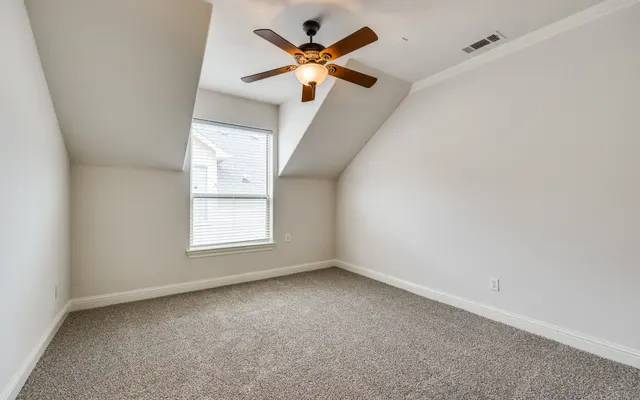 Minimalist Room with Ceiling Fan A sparsely furnished room with carpeted flooring, a ceiling fan, and a slanted ceiling. There is a window allowing natural light to enter the space.