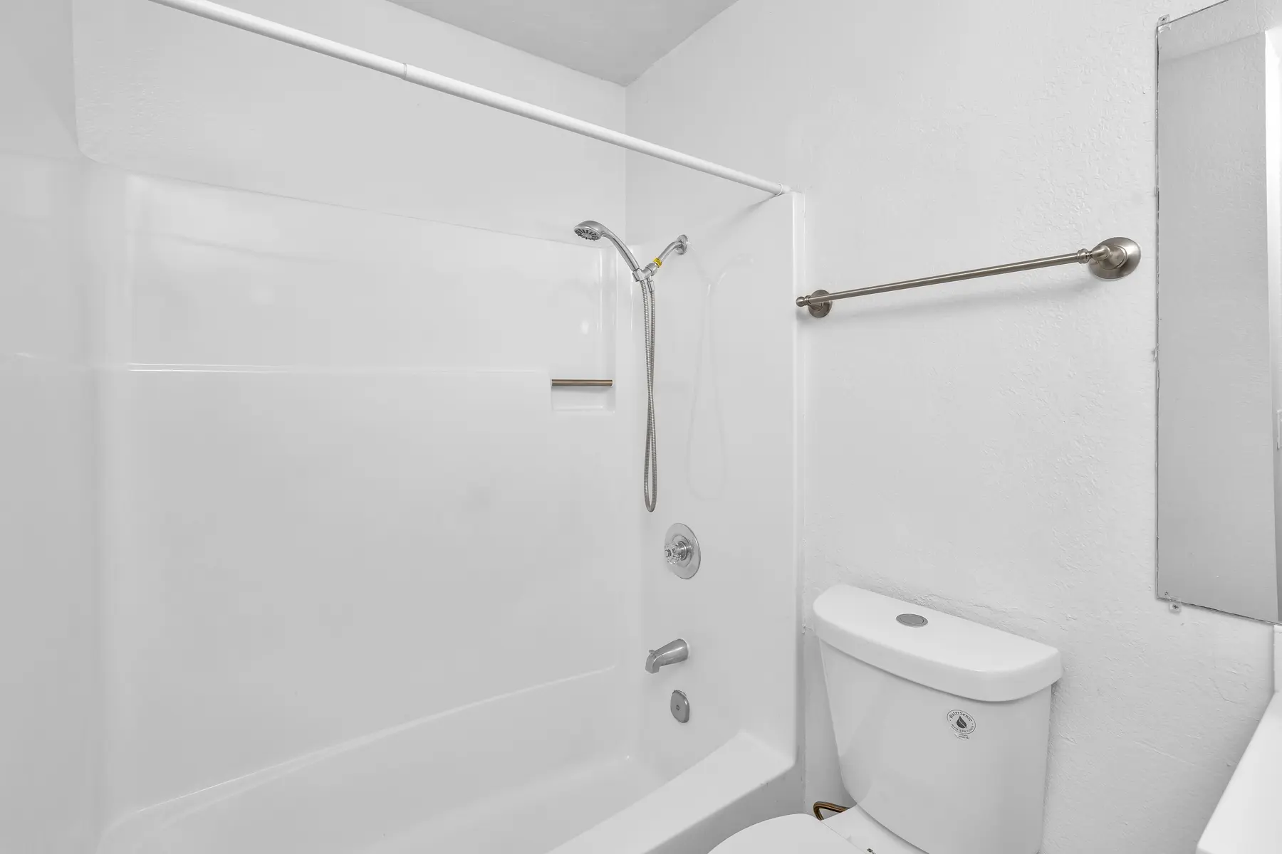 A clean, minimalist bathroom featuring a shower with a bath tub on one side and a toilet on the other. The walls and surfaces are white, contributing to a bright and airy ambiance.