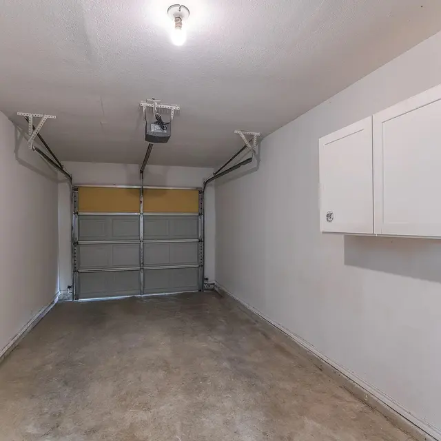 Interior view of an empty garage with concrete flooring, a garage door, and wall cabinets.
