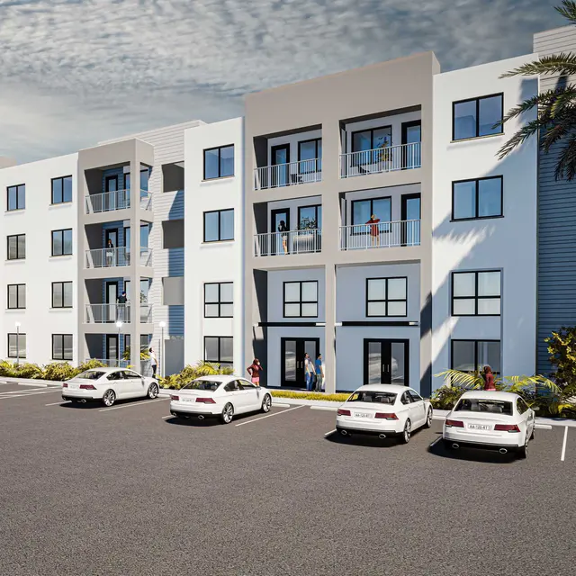 A modern apartment complex with three floors, featuring large windows and a parking lot filled with white cars. Palm trees are visible in the foreground, and the sky is partly cloudy.