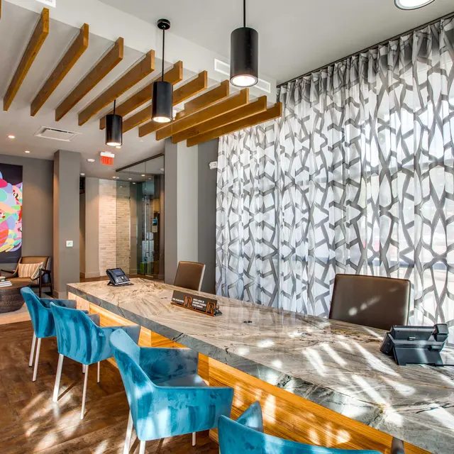 A modern reception area featuring a sleek marble counter with blue chairs, artistic wall decor, and decorative lighting fixtures.
