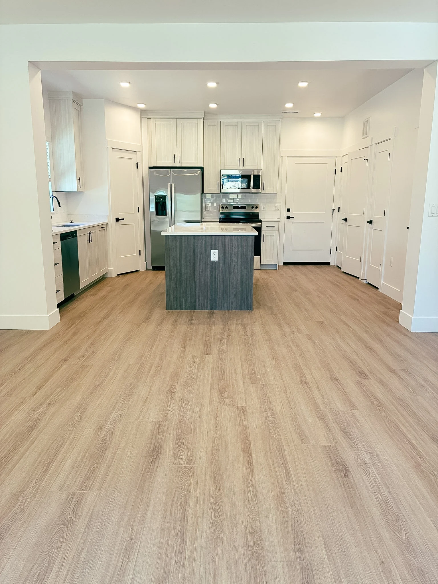 A contemporary kitchen interior featuring a central island, modern appliances, and light wood flooring.