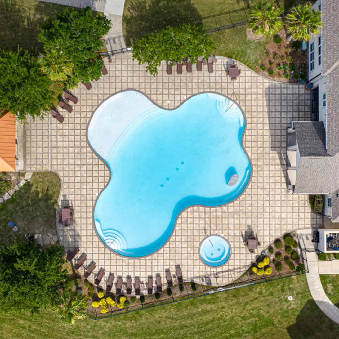 Aerial view of a large, kidney-shaped swimming pool surrounded by loungers and landscaped greenery.