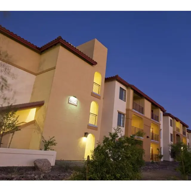 Evening Apartment Building An evening view of a multi-story apartment building with a light illuminating the entrance, surrounded by landscaping and trees.