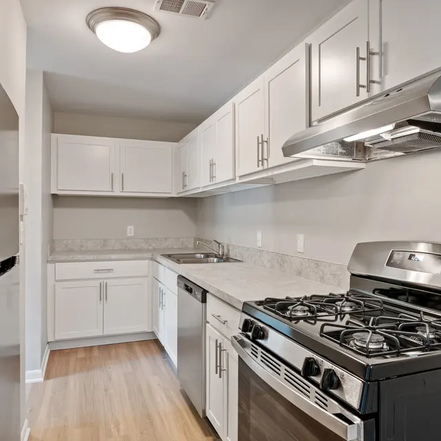 A modern kitchen featuring white cabinetry, stainless steel appliances, and a gas stove on a granite countertop.