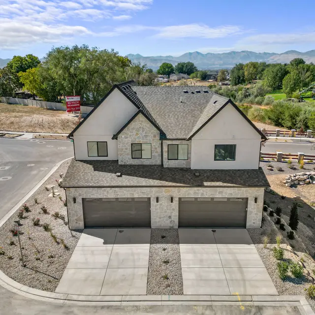 A modern two-story house with a stone exterior and a double garage, located at the end of a cul-de-sac with landscaping and mountains in the background.