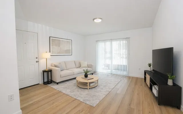 Modern Living Room Interior A modern living room featuring a beige sofa, a round coffee table, a TV cabinet with a television, and a door leading to an outdoor space. Large windows allow natural light to flood the room.
