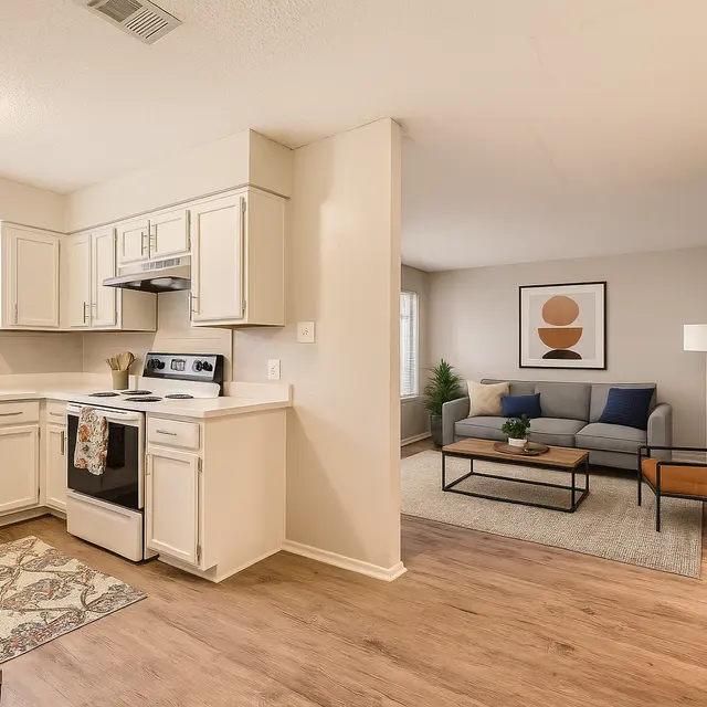 View of a modern kitchen connected to a cozy living room area. The kitchen features white cabinets and stainless steel appliances, while the living room has a stylish sofa, a chair, and decorative art on the walls.