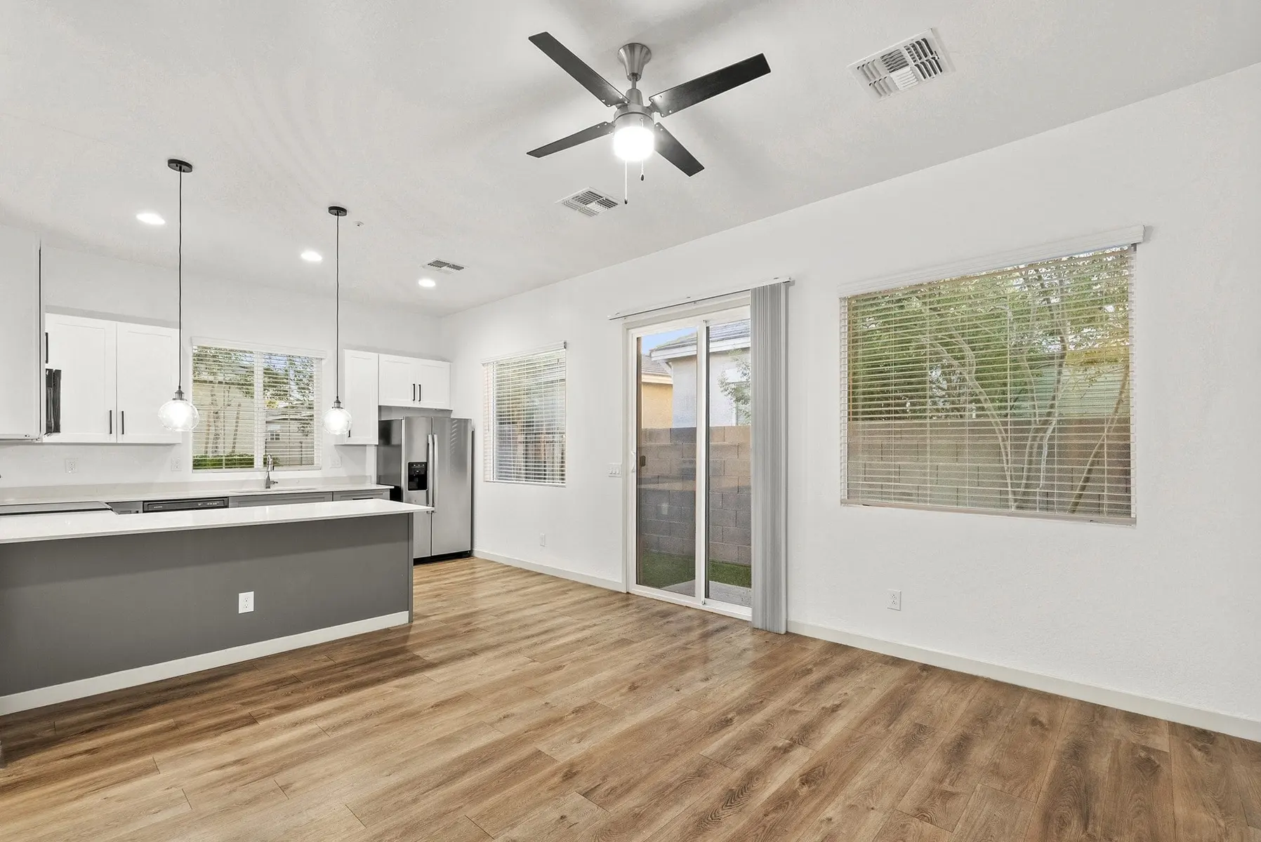 Modern kitchen and living area with light wood flooring, white cabinets, large windows, and a sliding glass door.