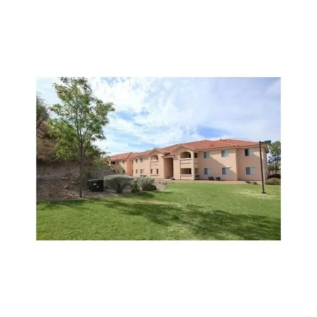 Apartment Complex Exterior View Exterior view of an apartment building surrounded by grass and trees, with a clear blue sky in the background.