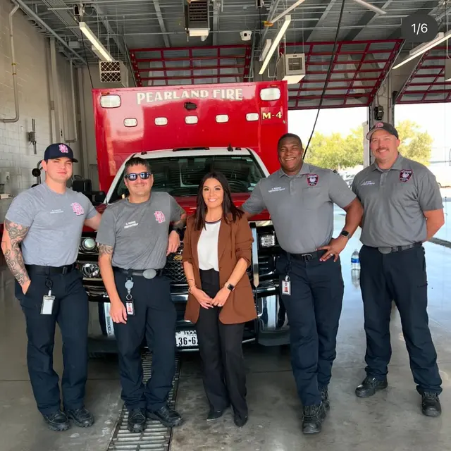 Firefighters at Pearland Fire Department A group of five individuals, four firefighters in uniform and one woman in business attire, posing in front of a fire truck at a fire station.