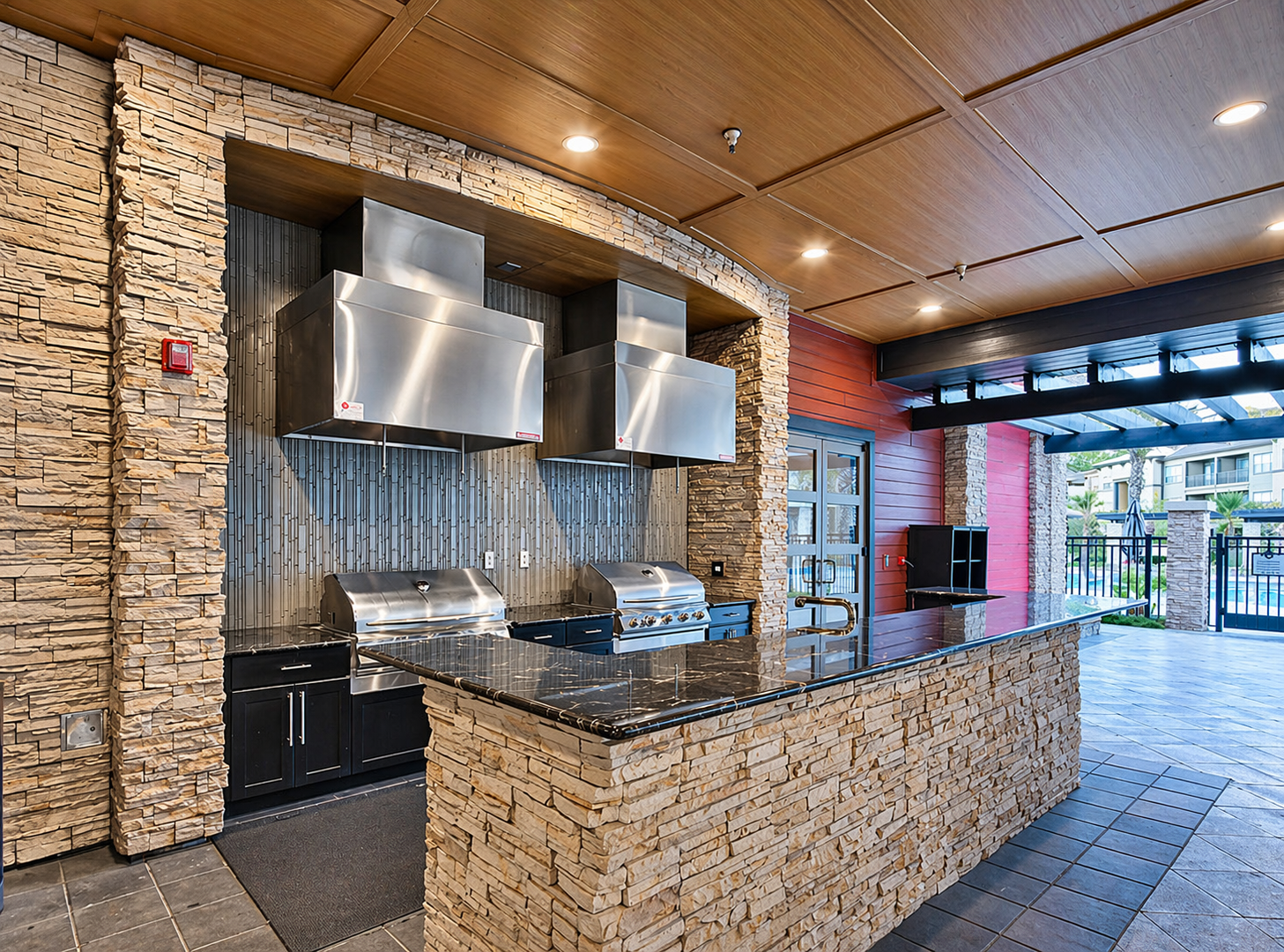 A modern outdoor kitchen area featuring stone walls, stainless steel appliances, and a granite countertop.