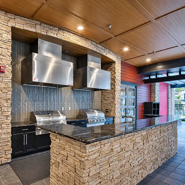 A modern outdoor kitchen area featuring stone walls, stainless steel appliances, and a granite countertop.