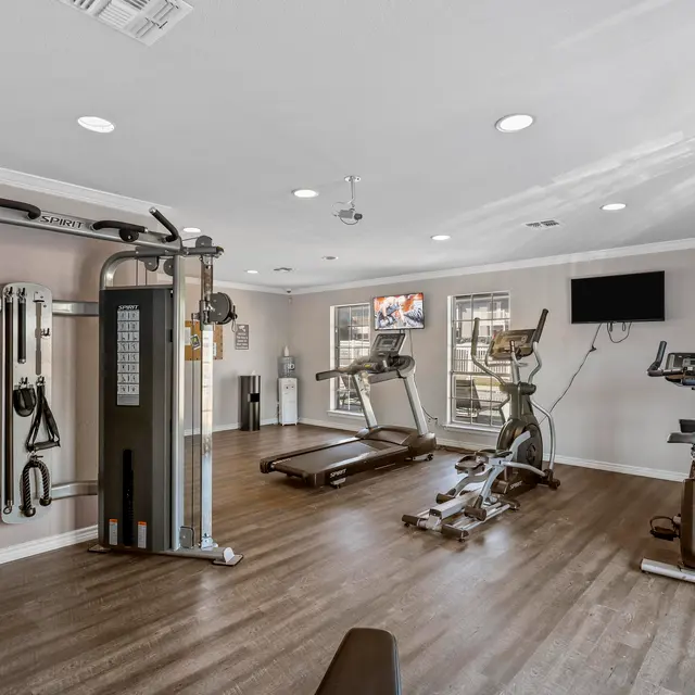 Interior view of a modern gym featuring various exercise equipment including multi-gyms, treadmills, and a monitor on the wall.