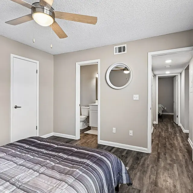 Modern Bedroom Interior A modern bedroom featuring a striped bedspread, a ceiling fan, a doorway leading to a bathroom, and a hallway visible in the background.