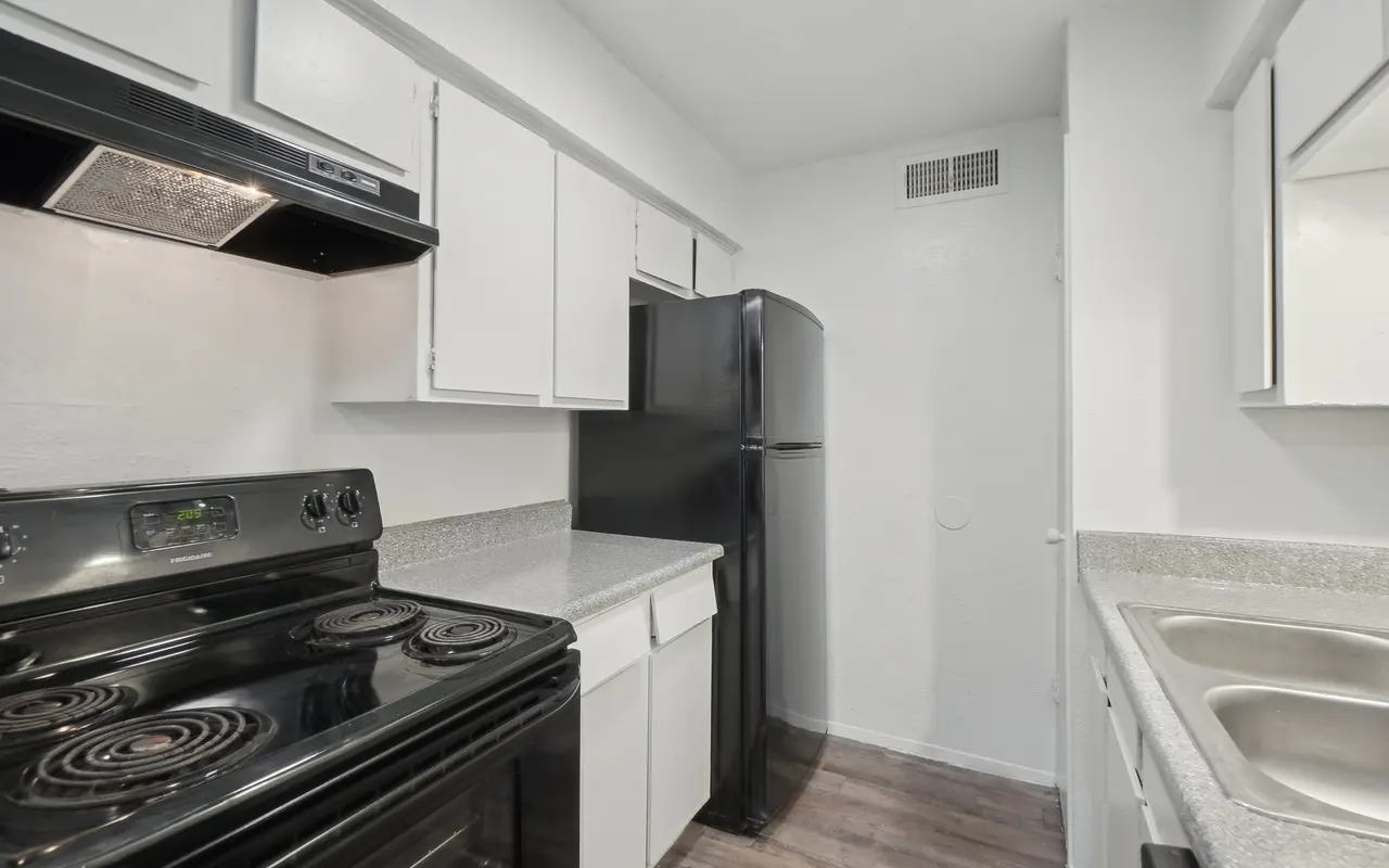 A modern kitchen featuring a black stove, refrigerator, and light-colored cabinets with a countertop.