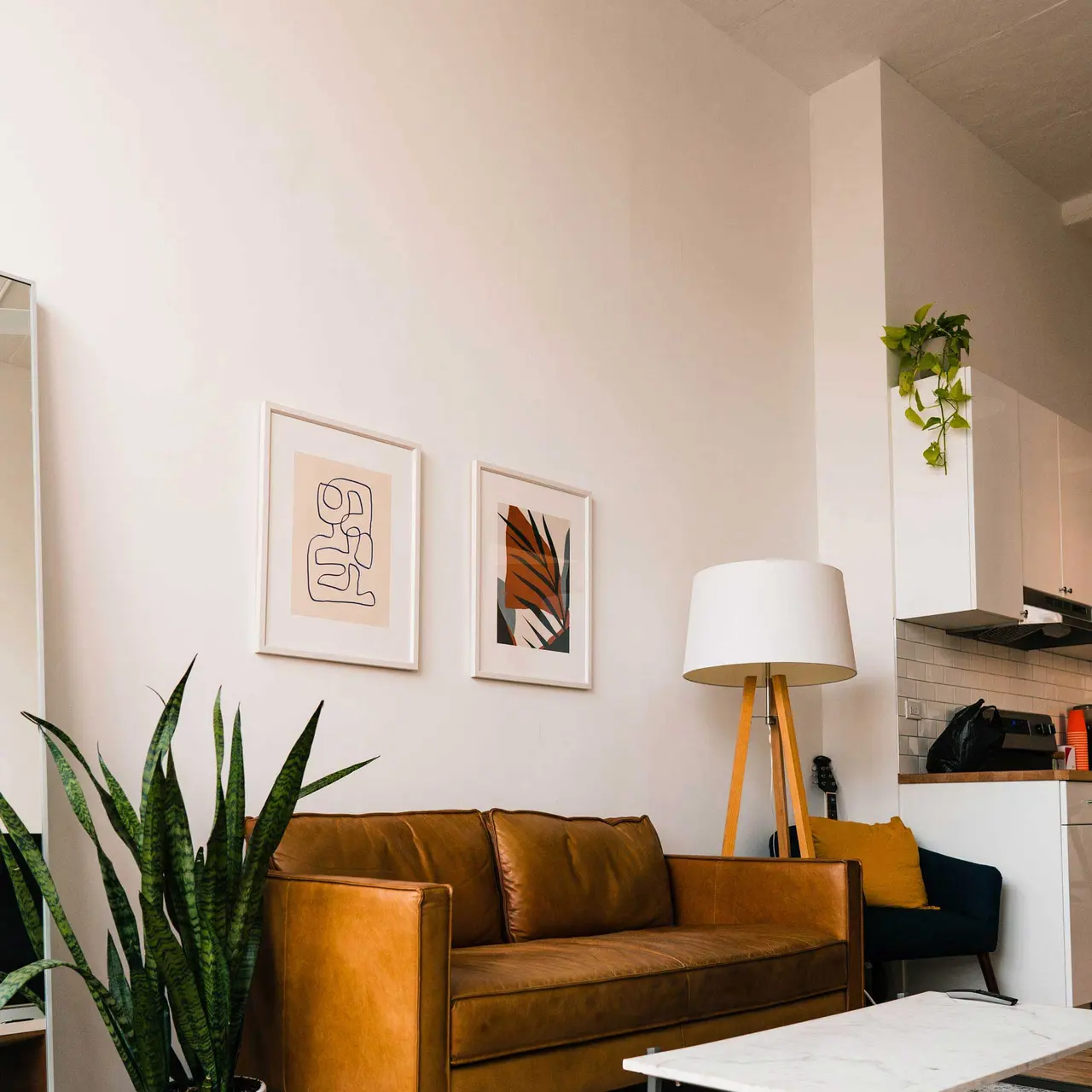Modern Living Room Interior A modern living room featuring a brown leather sofa, white coffee table, indoor plants, and decorative wall art. The space is bright and airy with a ceiling fan.