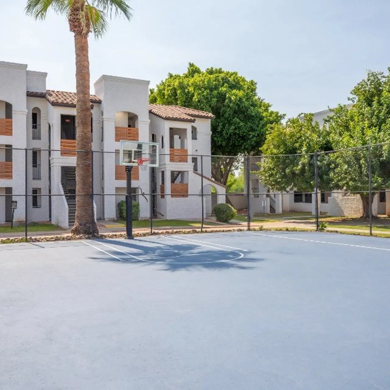 A basketball court in front of a residential apartment complex with palm trees and greenery.