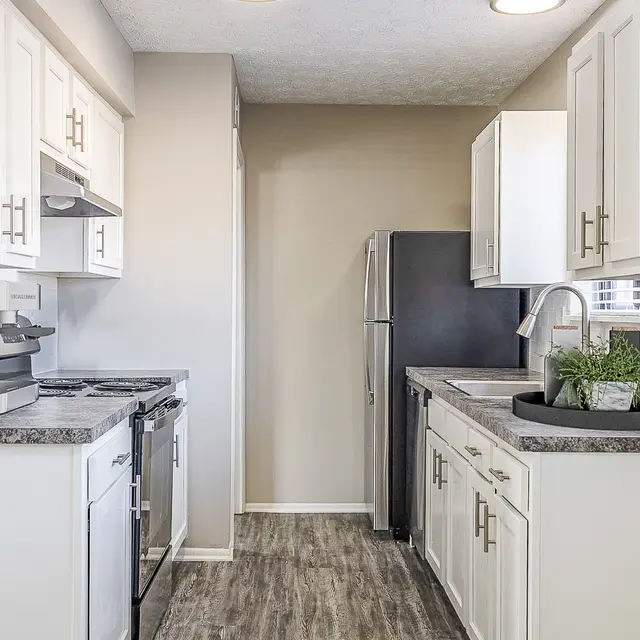 The Hideaway -  A modern kitchen with white cabinets, stainless steel appliances, and a grey countertop. There is a coffee machine on the counter and a refrigerator on the right.