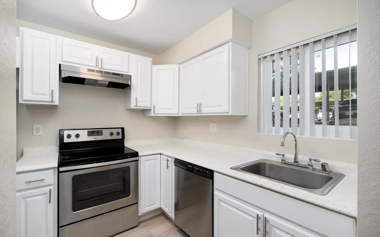 A modern kitchen featuring white cabinets, a black stove, stainless steel appliances, and a sink with a window.