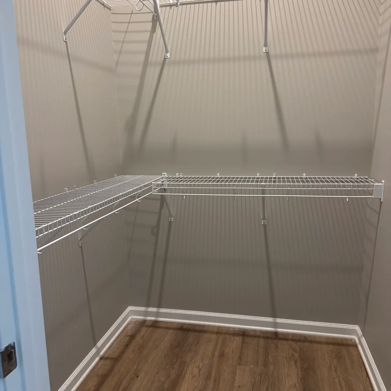 An empty closet with wire shelving installed on the walls, showcasing a spacious area with wooden flooring.