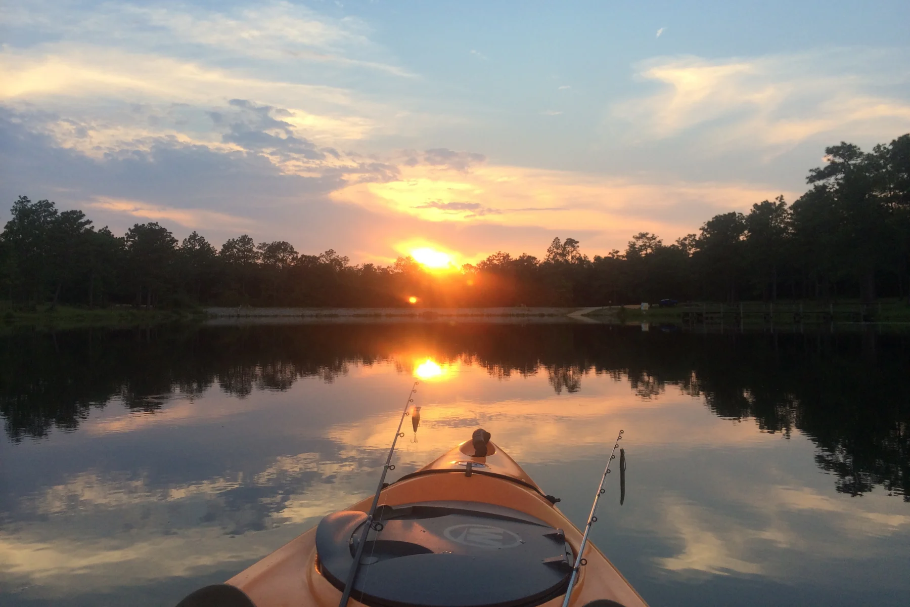 Sunset Reflections from a Kayak A scenic view from a kayak, showcasing a vibrant sunset reflected on calm waters surrounded by trees.