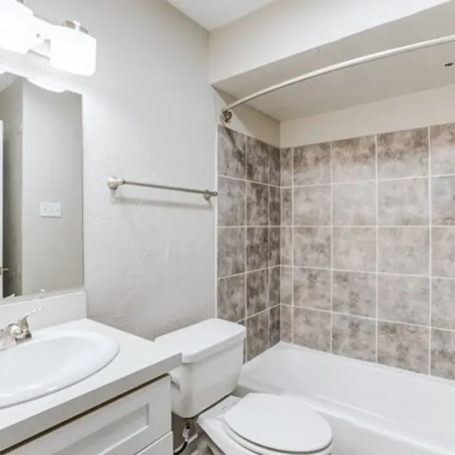 Modern bathroom featuring a bathtub, toilet, and sink with a light-colored tile wall.