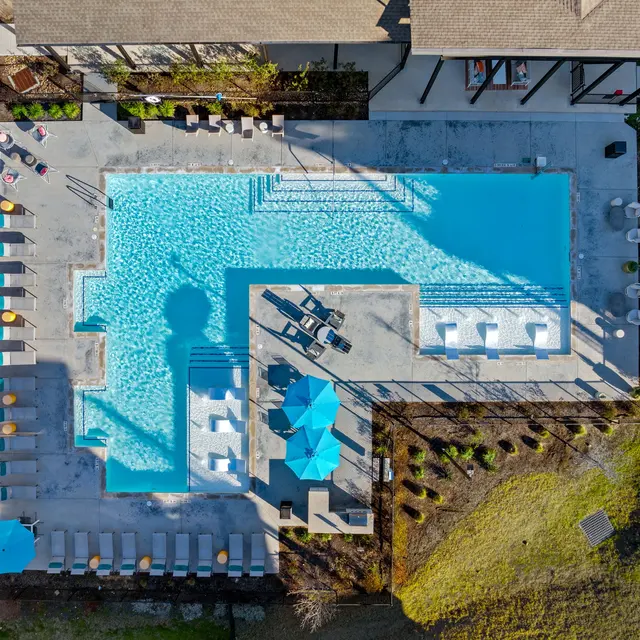 Aerial view of a rectangular swimming pool surrounded by lounge chairs and umbrellas, with landscaped areas and pathways nearby.