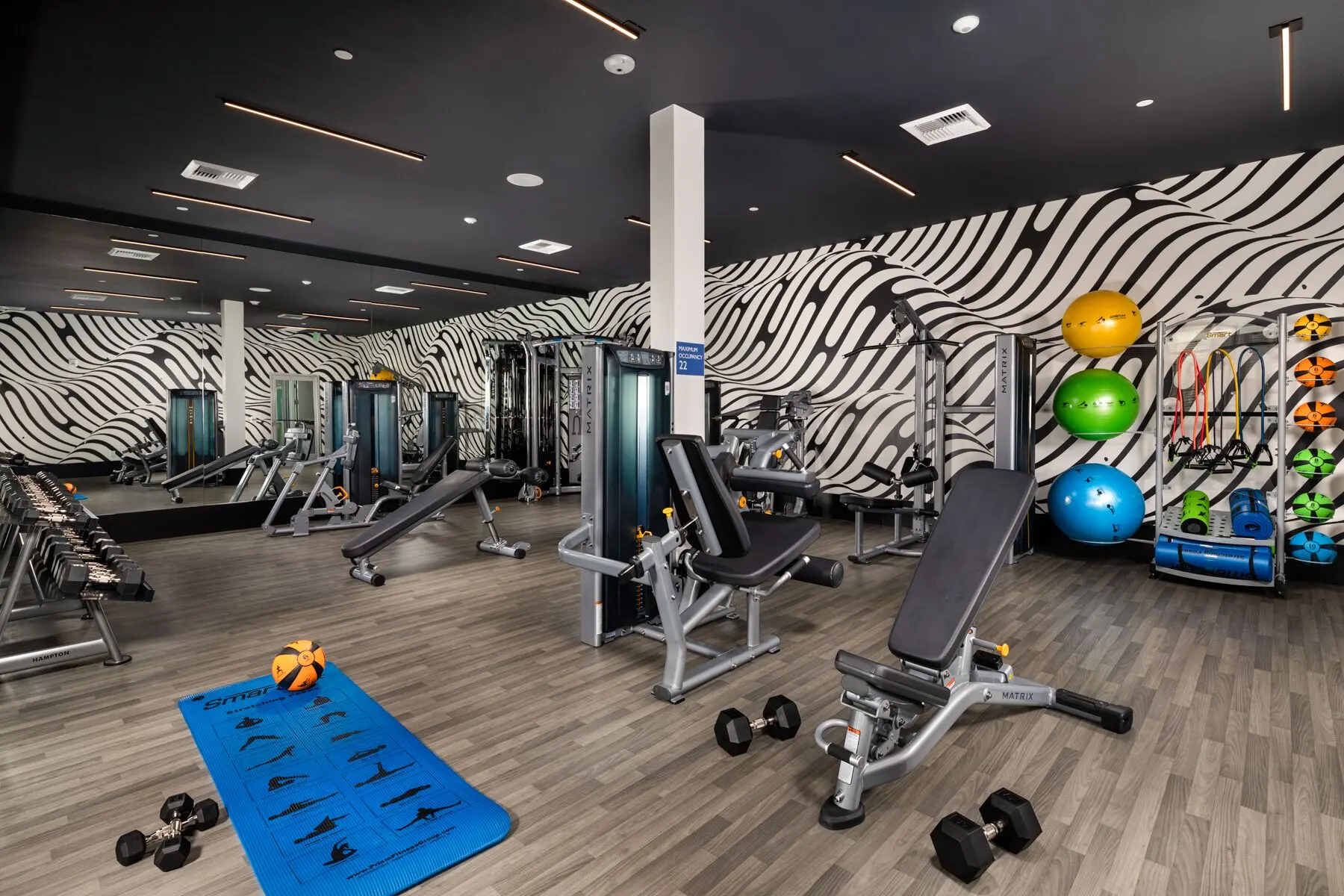 Interior of a modern gym featuring workout equipment and fitness accessories, with a stylish striped wall design.