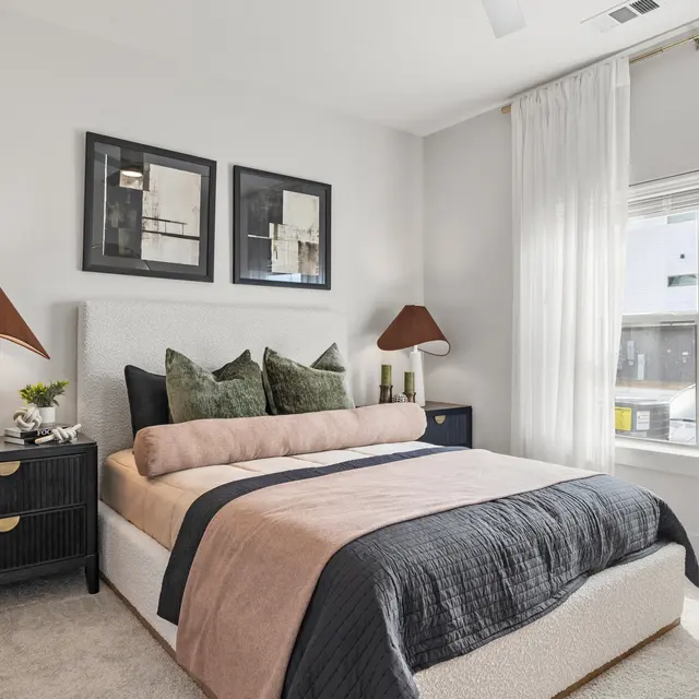 A stylish modern bedroom featuring a large bed with decorative pillows, two lamps on nightstands, and art on the wall.