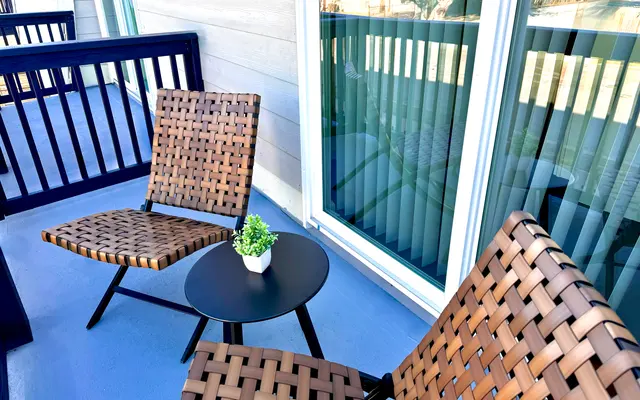 Cozy Balcony Seating Area A cozy balcony setup featuring two woven chairs and a small round table with a potted plant on it, surrounded by large windows.