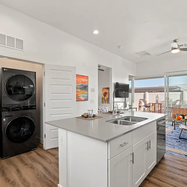 Modern kitchen and living area in an apartment, featuring a washer and dryer, open layout, and a patio door.