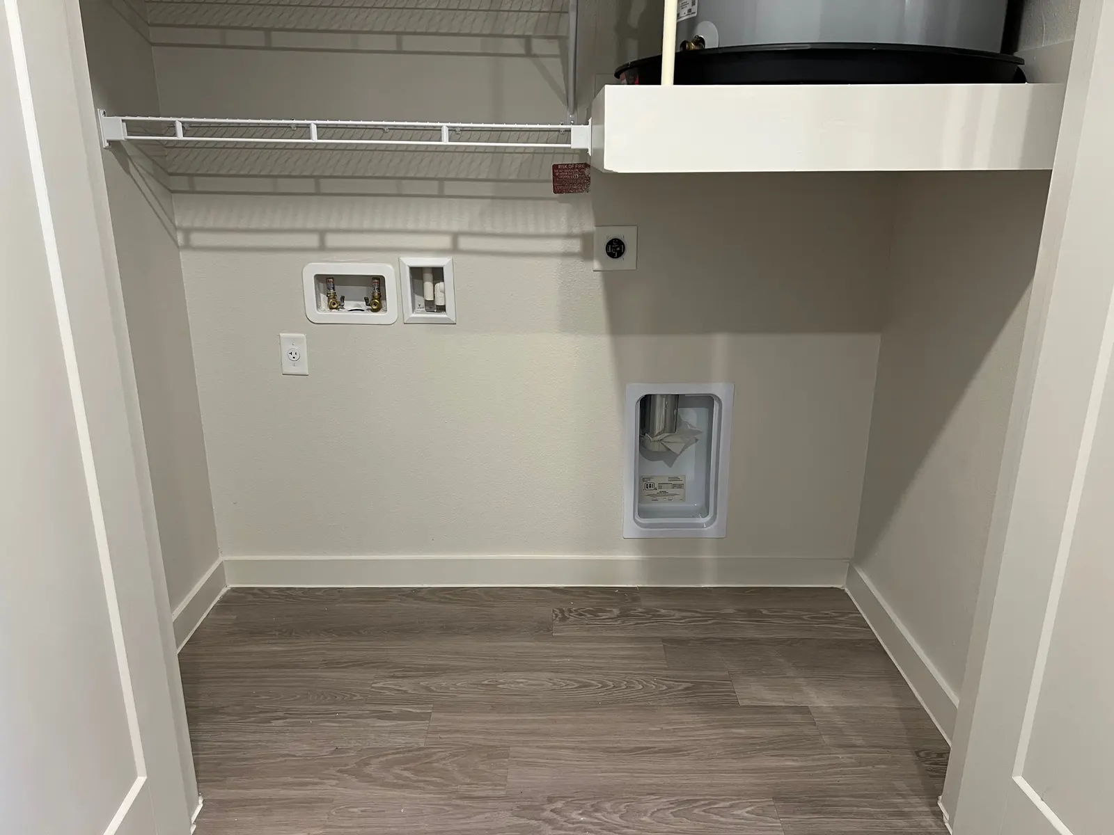 Empty Closet Space An empty closet space featuring laminate flooring, wall-mounted shelves, and a small water access point.