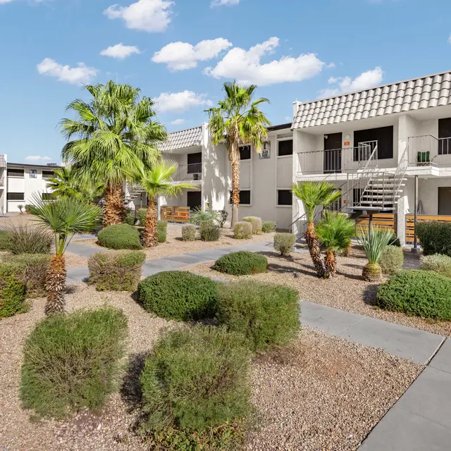 A view of an apartment complex courtyard featuring palm trees, greenery, and two-story buildings.