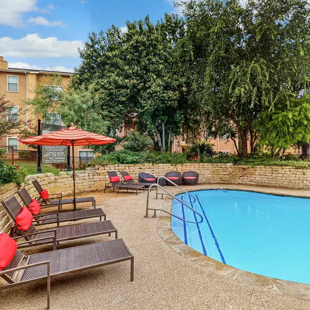 A scenic residential pool area featuring a swimming pool surrounded by lounge chairs and umbrellas. Lush greenery and colorful flowers enhance the setting.