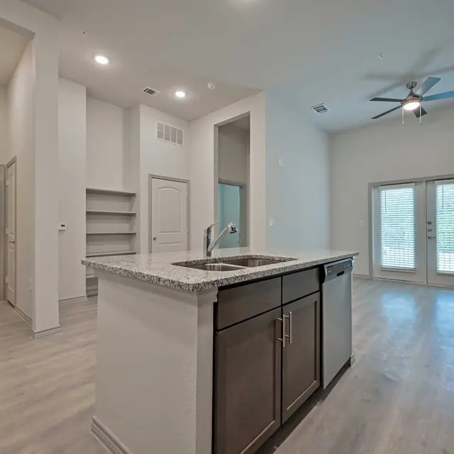 Interior view of a modern apartment featuring a kitchen island, light hardwood flooring, and natural light from large windows.
