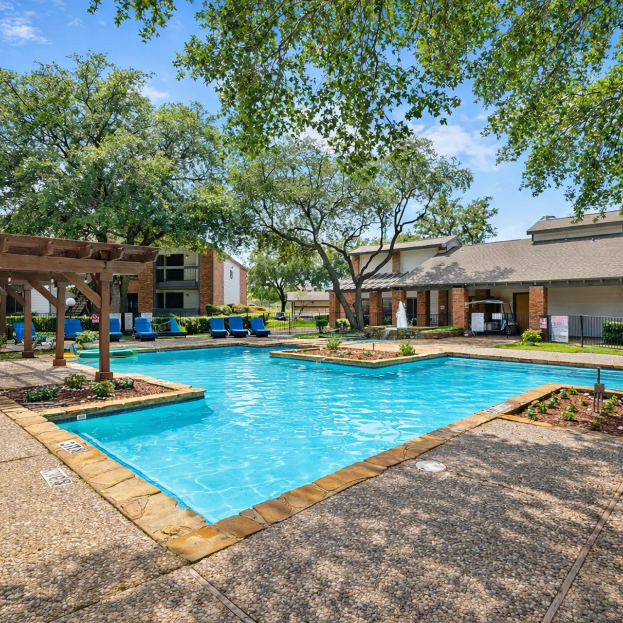 A swimming pool area featuring a clear blue pool surrounded by lounge chairs and shaded by trees.