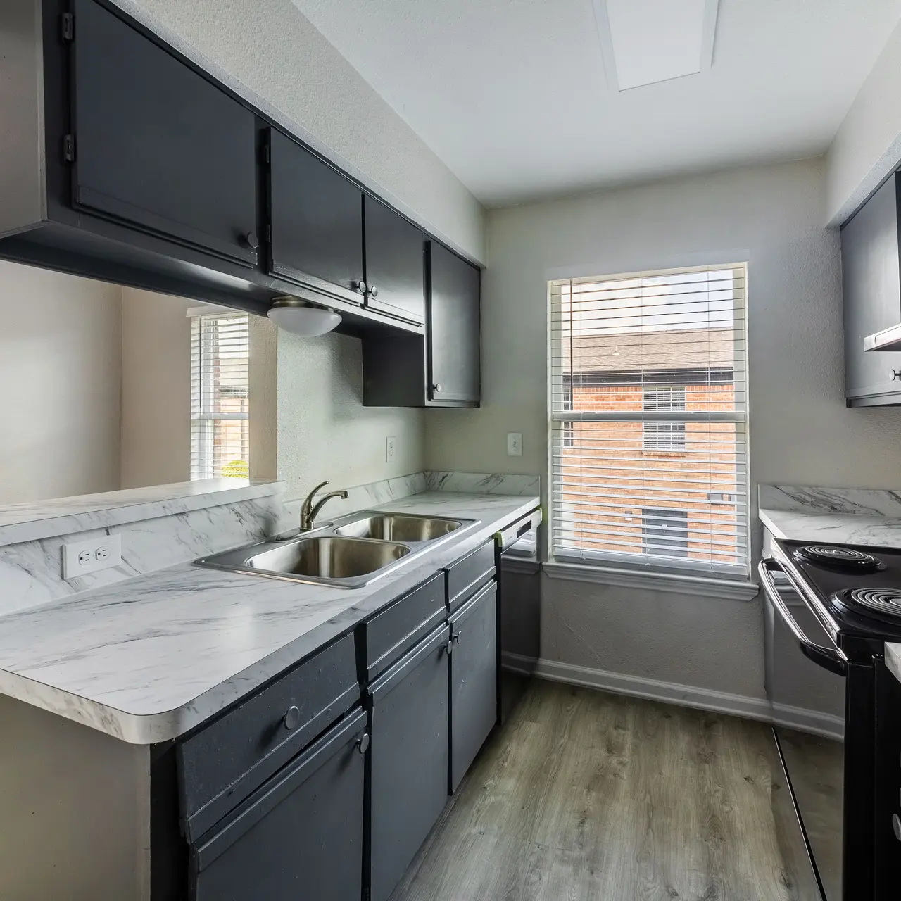 A bright and modern kitchen featuring black cabinets, a marble countertop with a double sink, and stainless steel appliances.