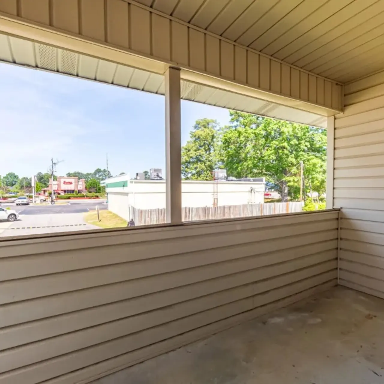 A view from an empty balcony overlooking a parking lot and surrounding buildings on a clear day.