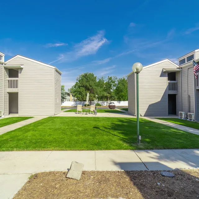 Apartment Complex Overview A view of a small apartment complex with two-story buildings on either side, surrounded by a grassy courtyard and blue sky.