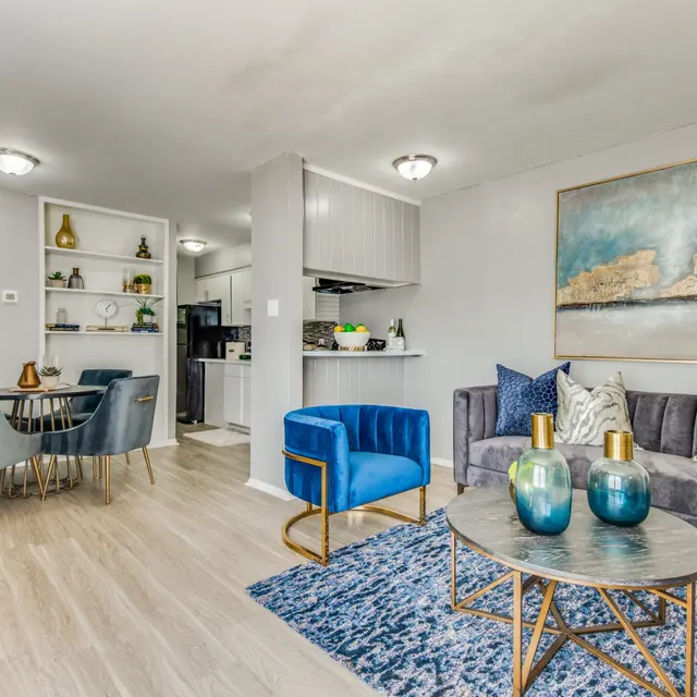 A modern living room with a dining area, featuring a gray couch, blue chairs, a round table, and decorative vases on a rug, showcasing a stylish and contemporary interior design.