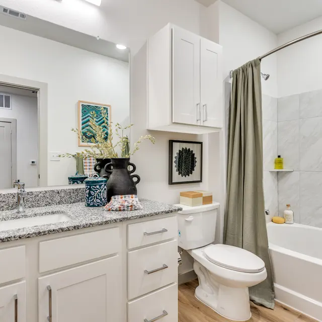 A modern bathroom featuring a bathtub and shower, white cabinets, and a granite countertop.