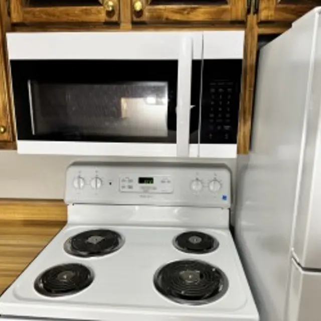 A kitchen featuring a white stove with four burners, a microwave mounted above it, and a section of wooden cabinetry.