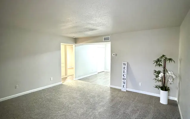 Spacious Living Room Interior A spacious living room with gray carpeting and beige walls, featuring an indoor plant and a decorative welcome sign.