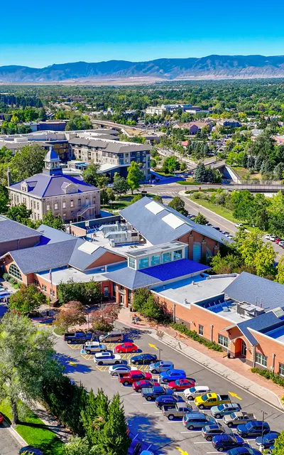 Aerial view of a city landscape featuring various buildings including a campus, surrounded by trees and mountains in the background.